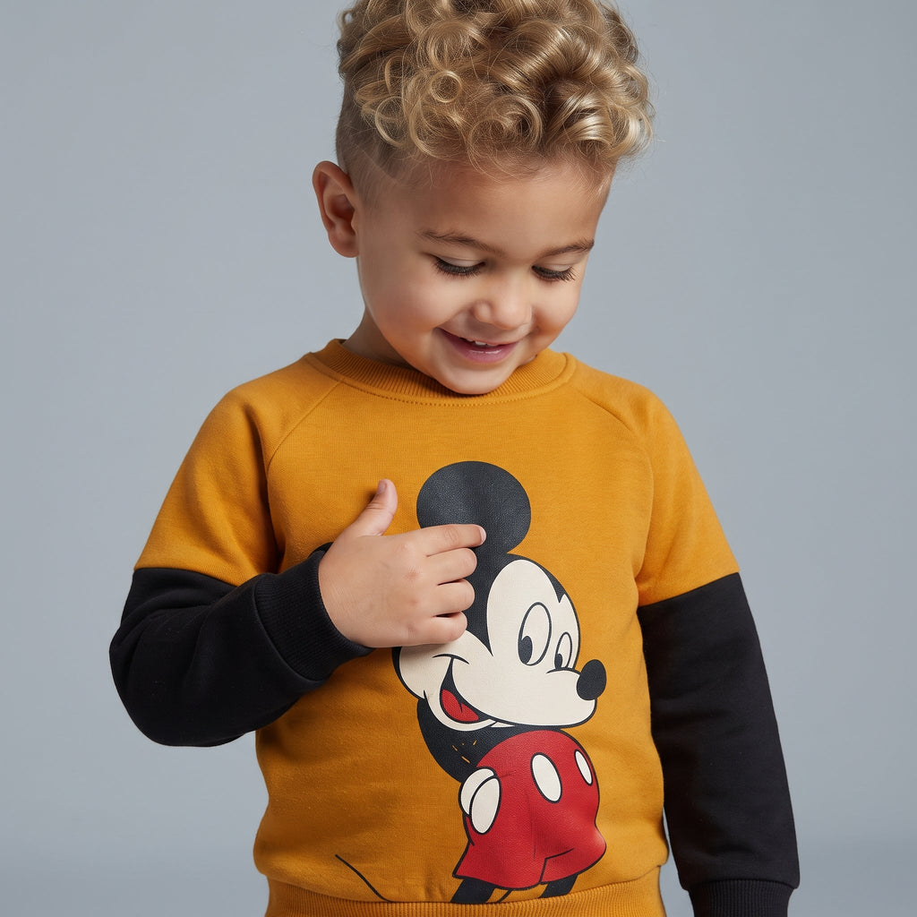 Niño sonriente vistiendo sudadera EmpiBy mostaza y negra con estampado de Mickey Mouse y mangas en contraste
