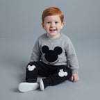 Niño pequeño sonriente con sudadera gris de Mickey Mouse y pantalón jogger negro con siluetas de EmpiBy