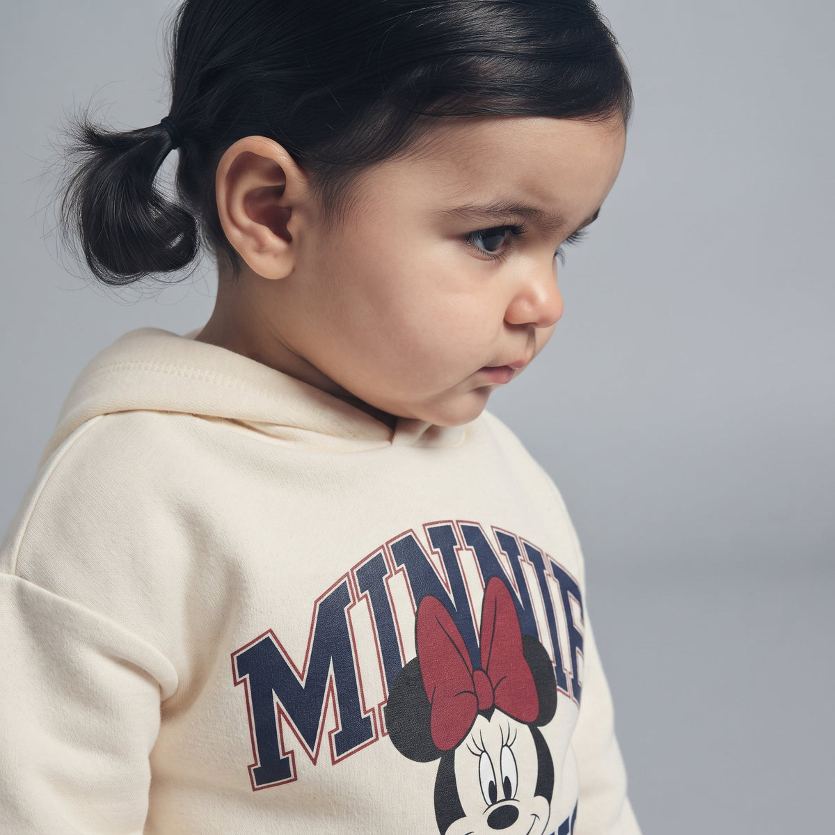 Niña pequeña vistiendo sudadera EmpiBy color crema con estampado de Minnie Mouse y capucha, vista de perfil.