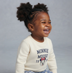 Niña sonriente vistiendo sudadera beige EmpiBy con estampado de Minnie Mouse y pantalón azul con flores