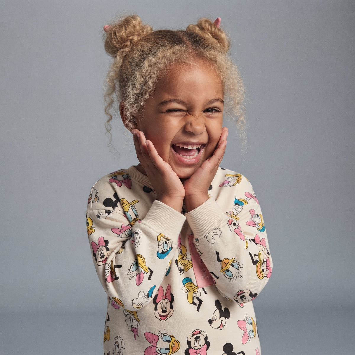Niña sonriente vistiendo sudadera EmpiBy con estampado de Minnie Mouse y amigos en tonos suaves y rosa salmón