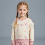 Niña con conjunto EmpiBy de sudadera crema con corazones rosas, volantes de encaje y lazos, estilo tierno y cómodo.