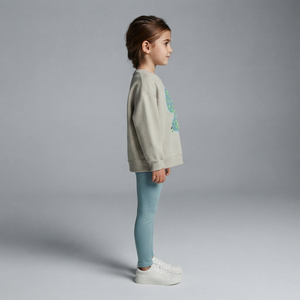 Niña de perfil vistiendo sudadera EmpiBy color crema con estampado de frutas y leggings azul claro