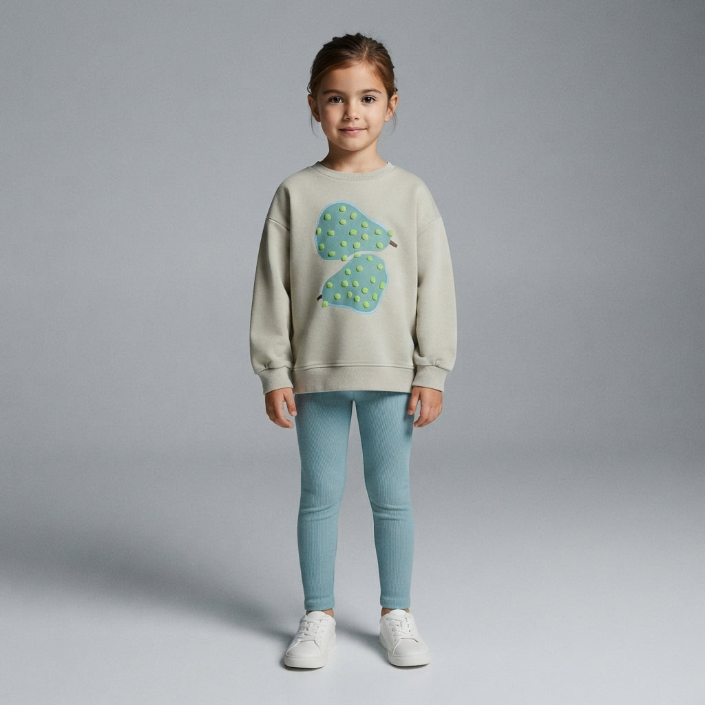 Niña vistiendo sudadera EmpiBy color beige con gráfico de peras y leggings azules, estilo casual y cómodo