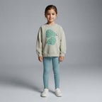 Niña vistiendo sudadera EmpiBy color beige con gráfico de peras y leggings azules, estilo casual y cómodo