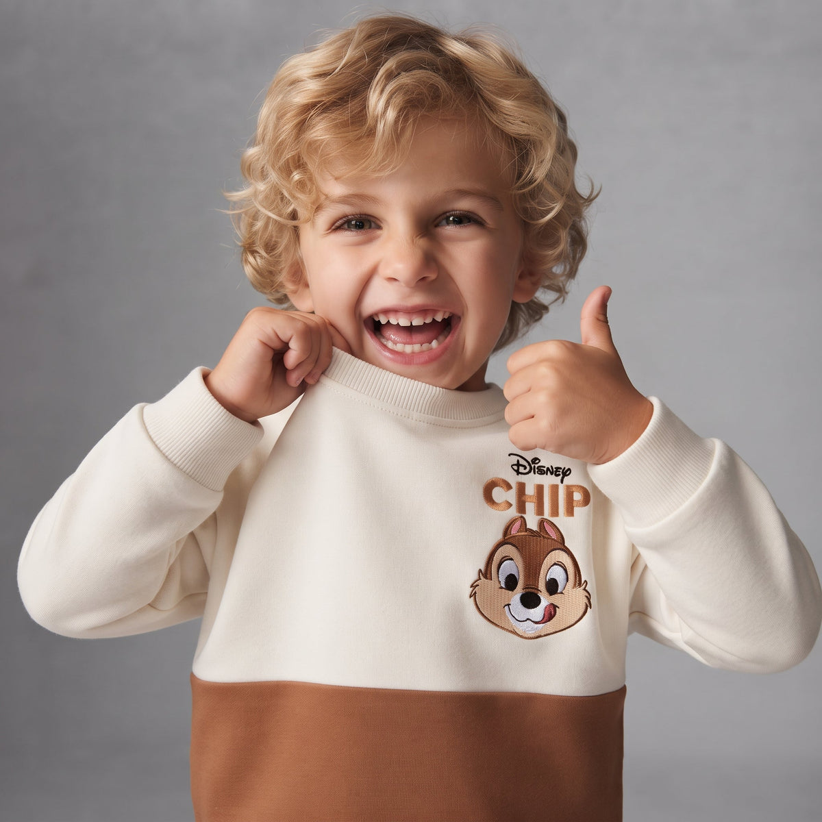 Niño sonriente vistiendo sudadera EmpiBy de Disney con estampado de Chip en color crema y marrón
