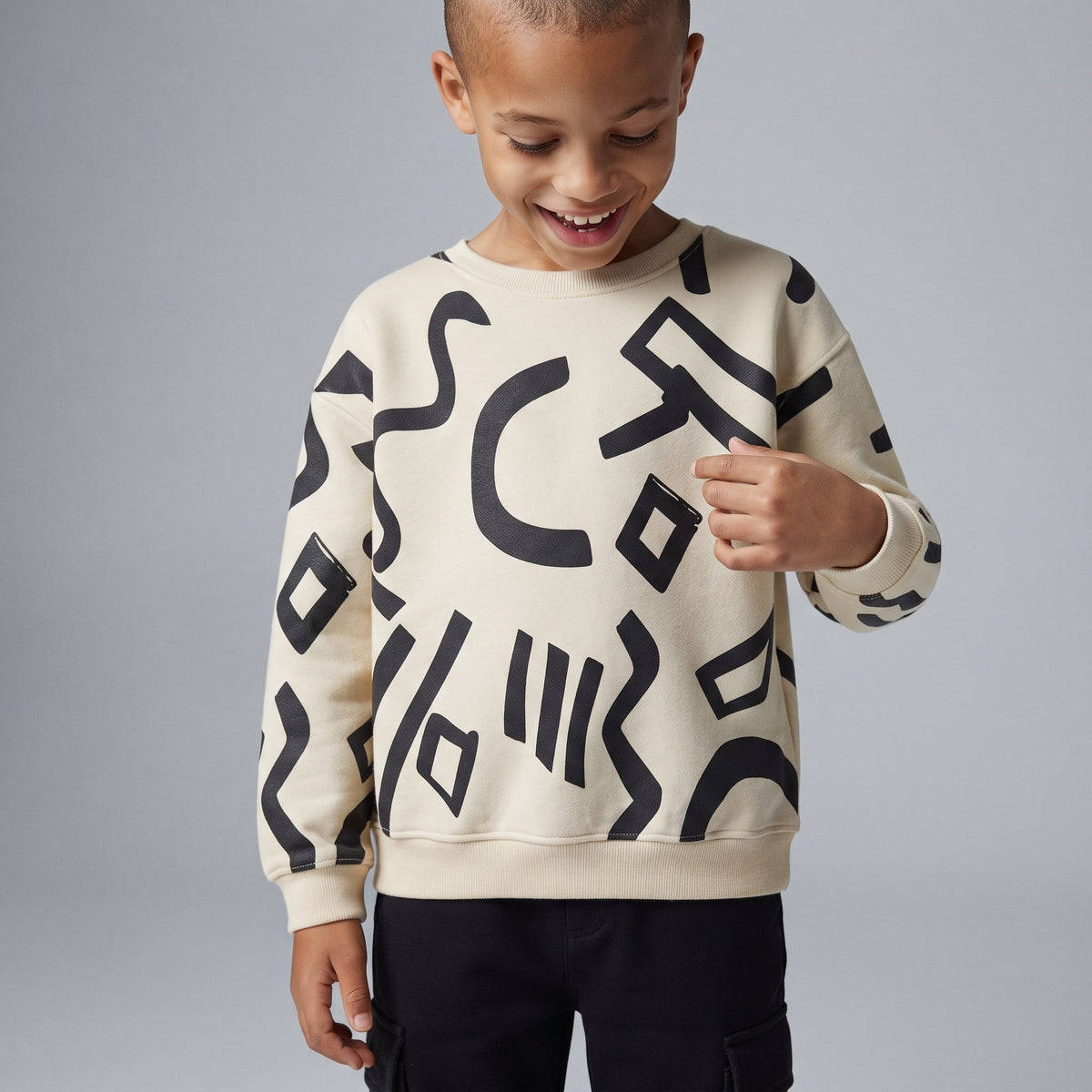 Niño vistiendo sudadera EmpiBy color marfil con estampado abstracto negro y pantalón jogger cargo a juego