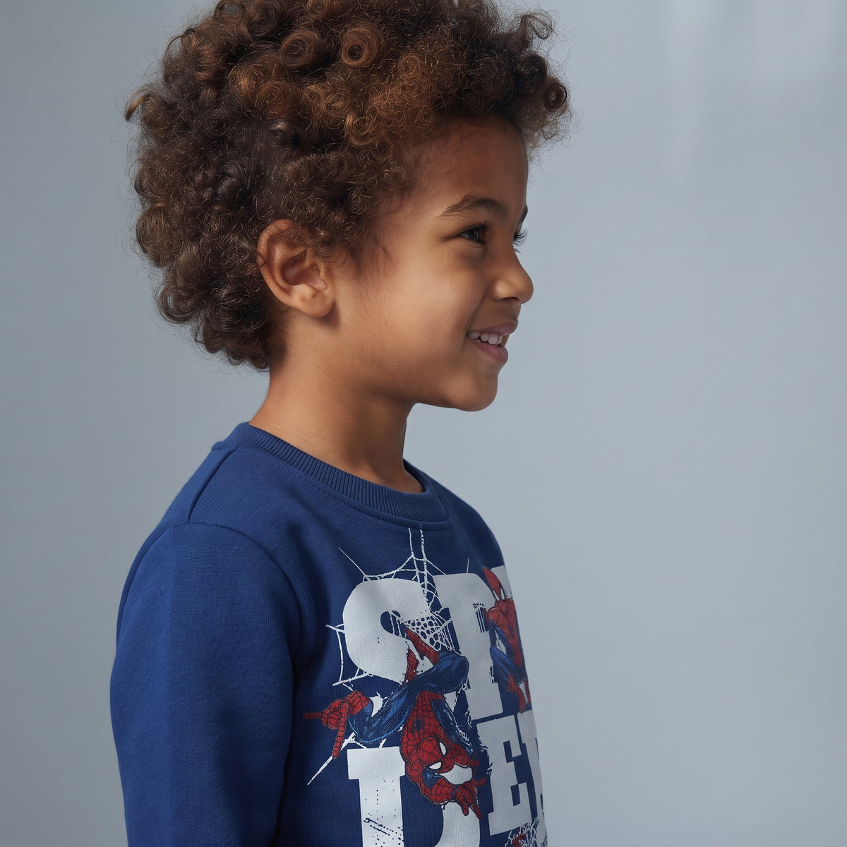 Niño sonriente vistiendo sudadera azul de Spider-Man de EmpiBy con estampado de superhéroe y telarañas