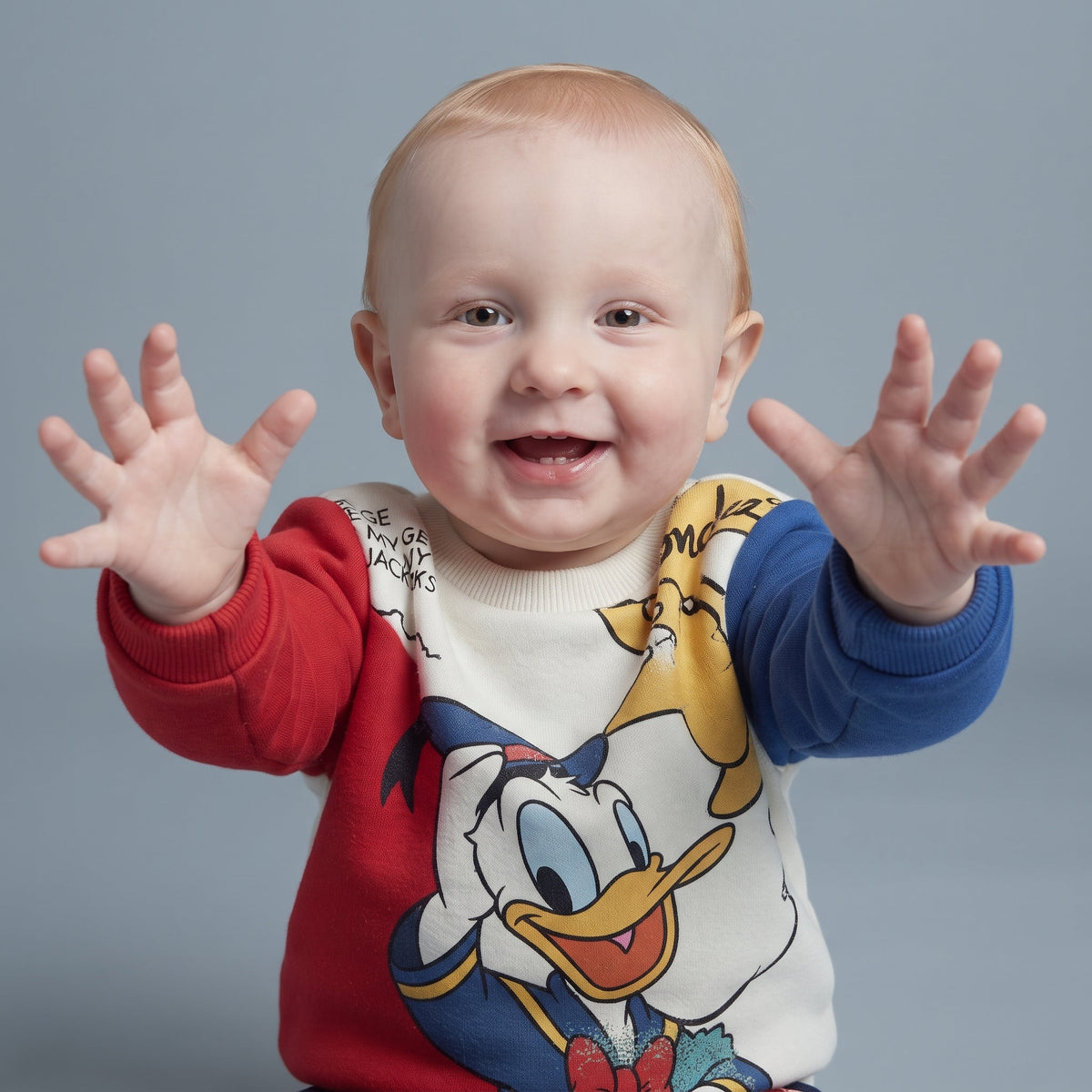 Bebé feliz vistiendo sudadera EmpiBy de Pato Donald con mangas rojas y azules, estilo cómodo y divertido.