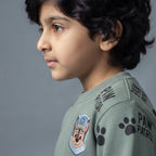 Niño vistiendo sudadera verde salvia EmpiBy con parche de Chase de Paw Patrol y estampado de huellas