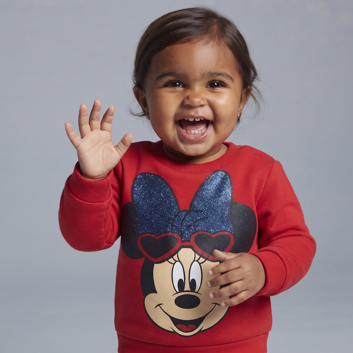 Niña pequeña sonriente vistiendo sudadera roja EmpiBy con estampado de Minnie Mouse y lazo azul brillante