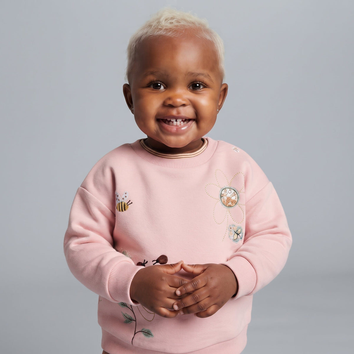 Bebé sonriente con sudadera rosa EmpiBy de cuello redondo, decorada con bordados de flores y abejitas en el frente.