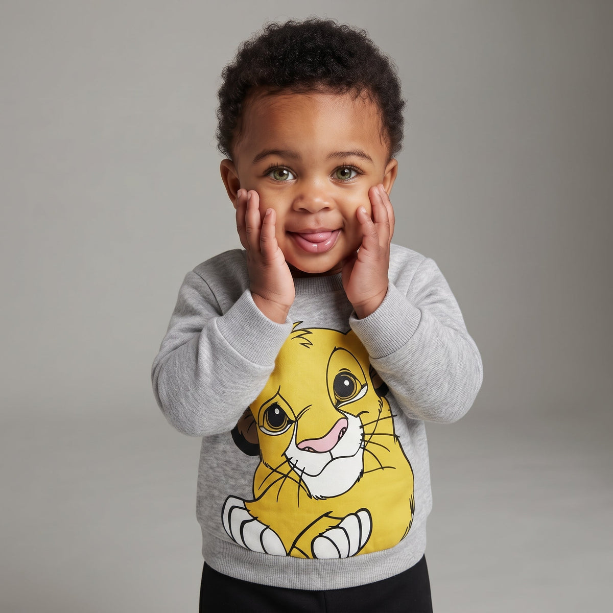Bebé sonriente vistiendo sudadera gris EmpiBy con estampado de Simba y pantalón negro, estilo casual y cómodo