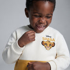 Niño riendo con sudadera EmpiBy de El Rey León en color crema y mostaza con bordado de Simba en el pecho