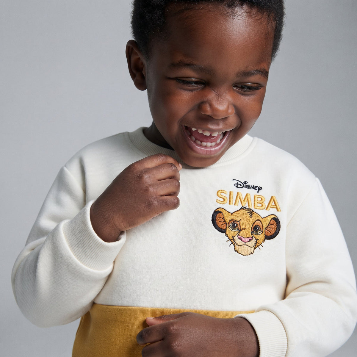 Niño riendo con sudadera EmpiBy de El Rey León en color crema y mostaza con bordado de Simba en el pecho