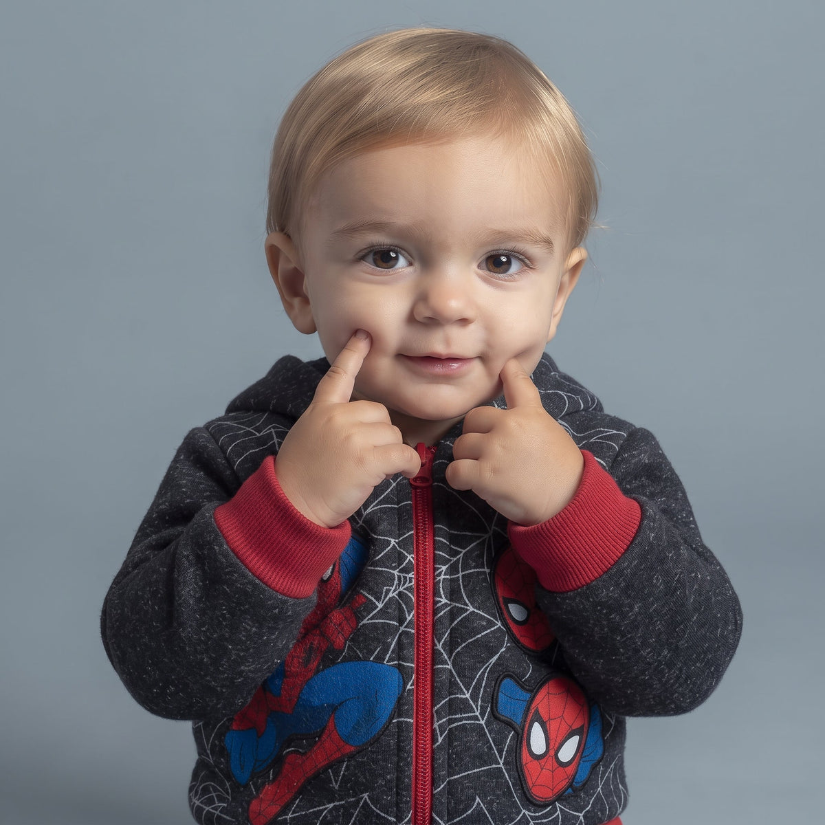 Bebé sonriente con sudadera gris de Spider-Man con cremallera y detalles rojos de la marca EmpiBy