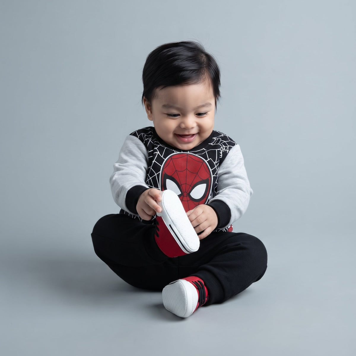 Bebé sonriente vistiendo conjunto EmpiBy de dos piezas de Spider-Man con sudadera gris y negra y pantalón jogger negro