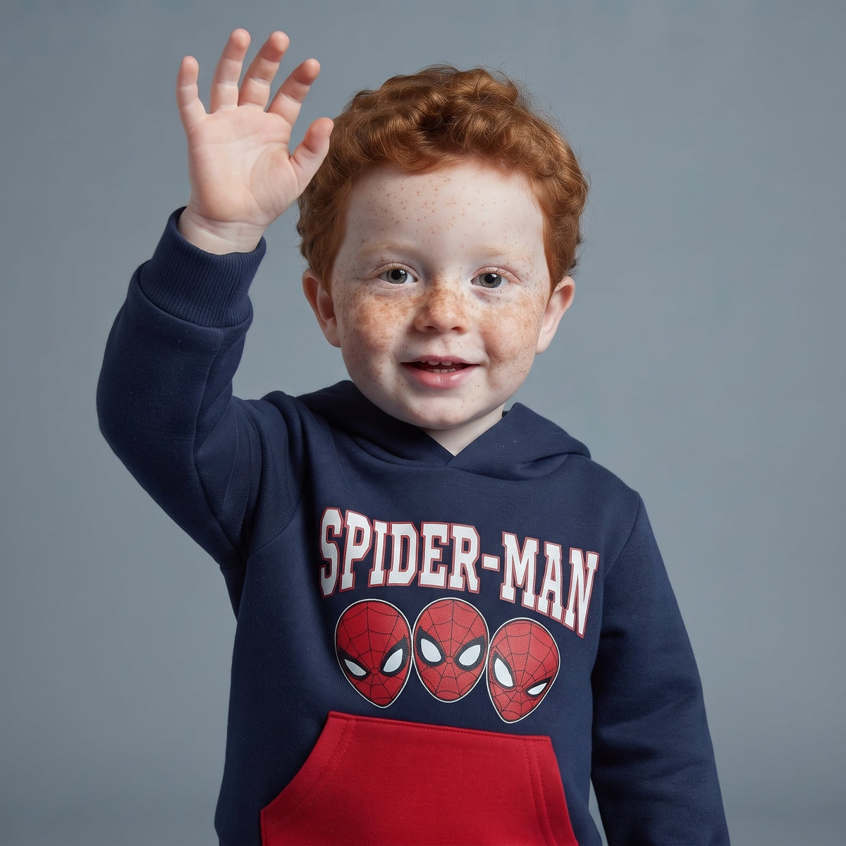 Niño pelirrojo con sudadera azul de Spider-Man con capucha y bolsillo rojo de EmpiBy saludando a la cámara