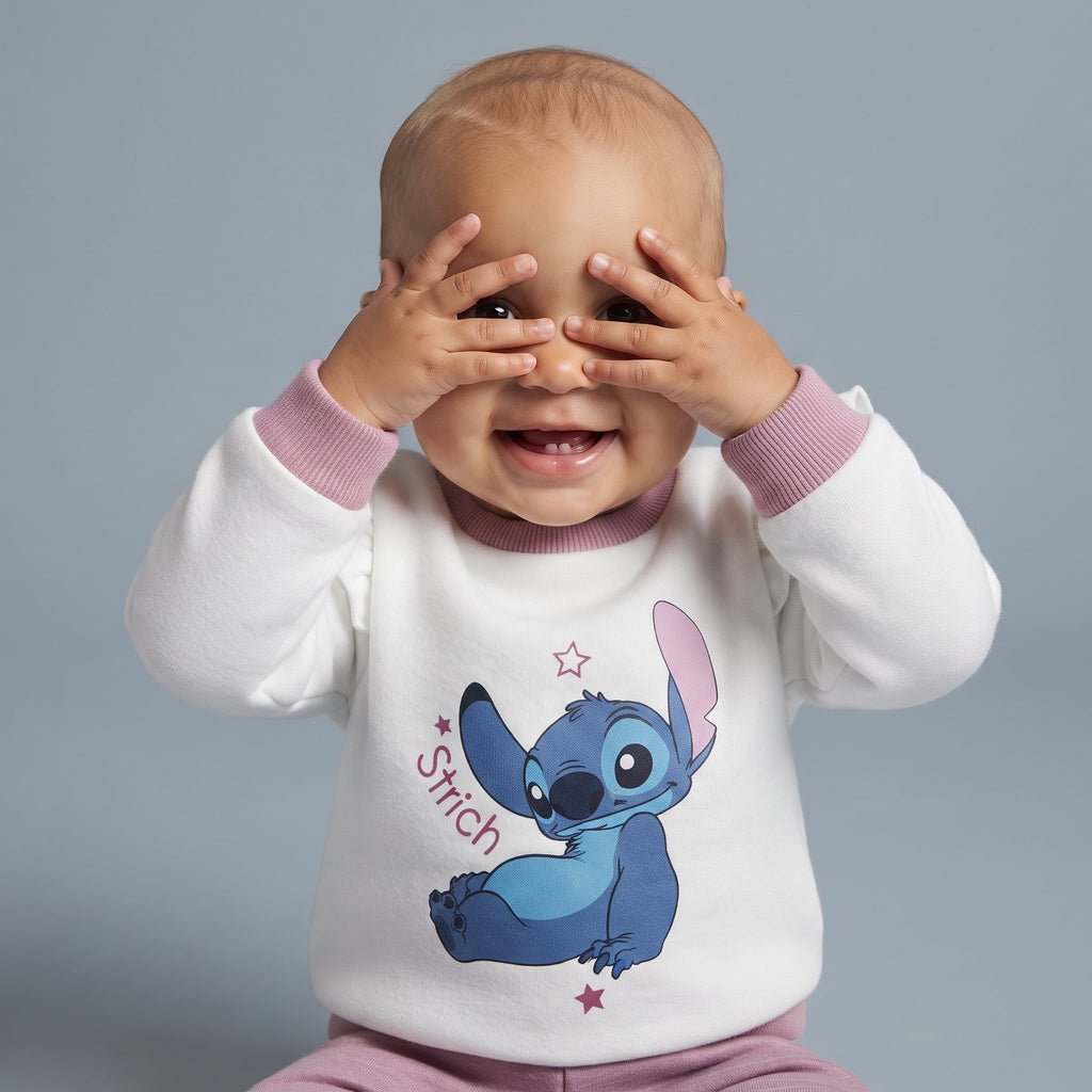 Bebé sonriente con las manos en la cara vistiendo sudadera blanca de Stitch con volantes de EmpiBy y pantalón malva