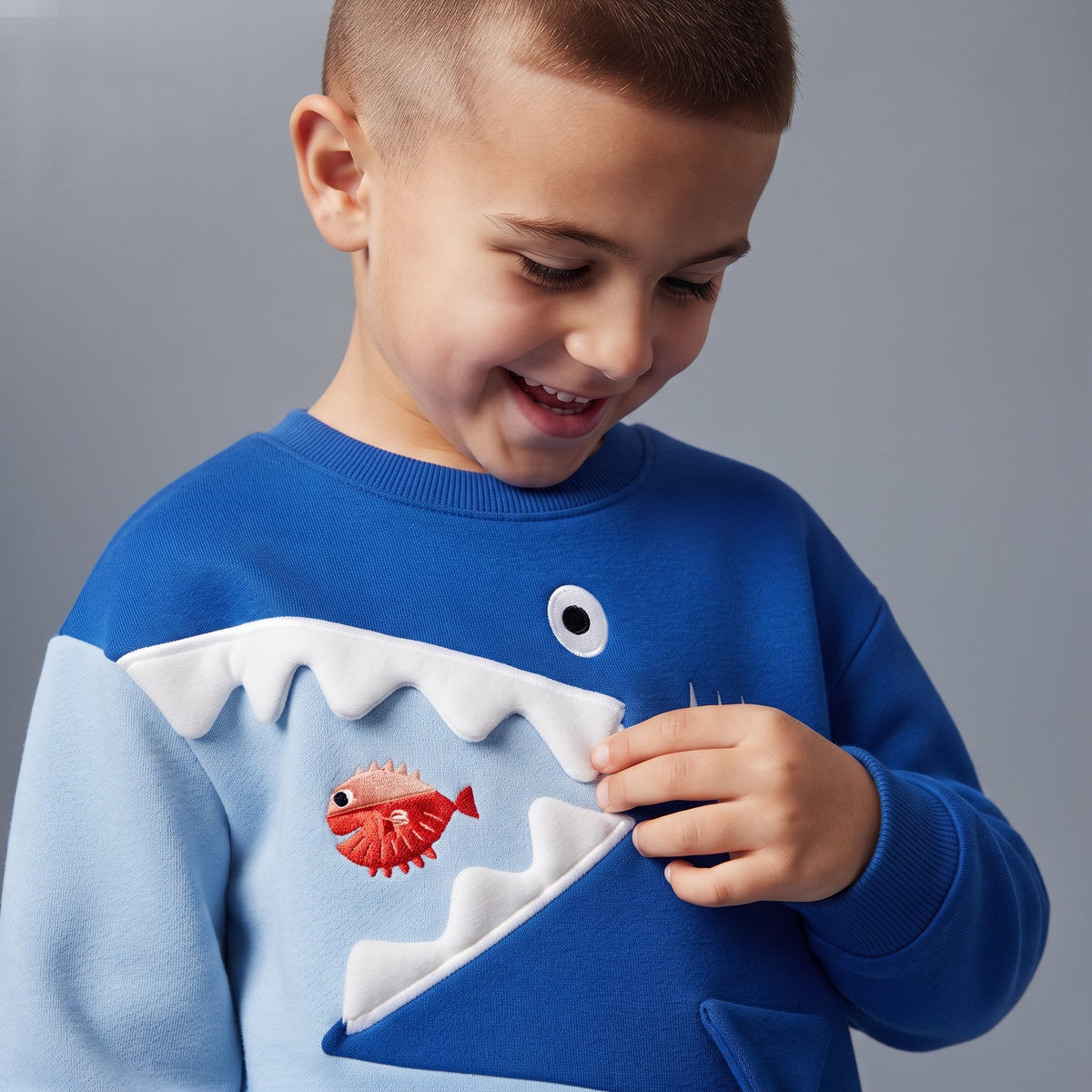Niño sonriente vistiendo sudadera EmpiBy azul con diseño de tiburón en relieve y detalles interactivos
