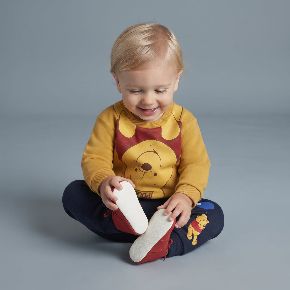 Bebé sonriente con conjunto EmpiBy de Winnie Pooh: buzo amarillo y pantalón jogger azul marino con estampado.