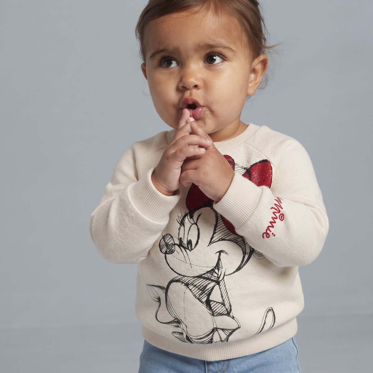 Niña pequeña vistiendo suéter EmpiBy color crema con estampado de Minnie Mouse y lazo rojo brillante