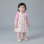 Niña pequeña con conjunto EmpiBy de vestido peto floral, camiseta rosa de manga larga, medias y zapatos a juego.