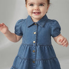 Bebé sonriente con vestido de mezclilla azul EmpiBy, mangas abullonadas, botones metálicos y detalle de oveja.