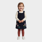 Niña sonriente con conjunto EmpiBy de vestido pichi azul marino de pana con bordado floral y camiseta de flores crema