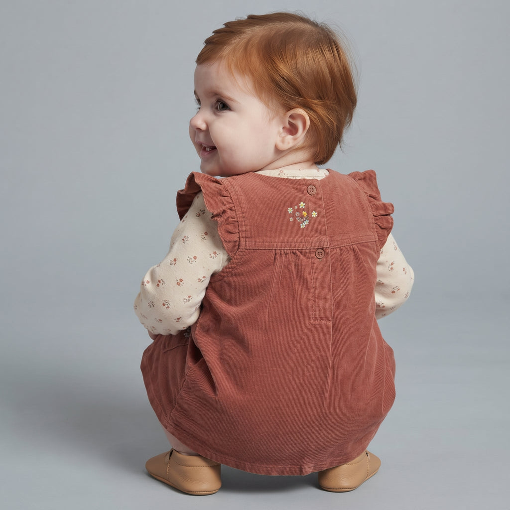 Bebé con conjunto EmpiBy de vestido peto de pana terracota y camiseta beige con flores, vista trasera