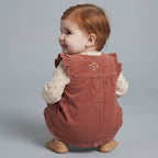 Bebé con conjunto EmpiBy de vestido peto de pana terracota y camiseta beige con flores, vista trasera