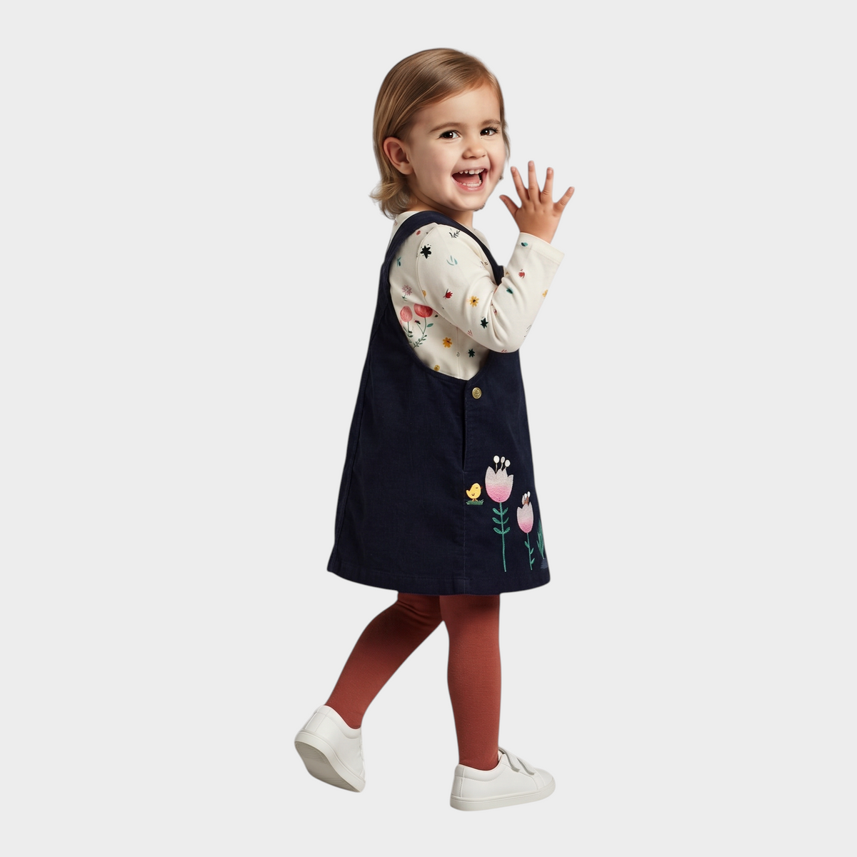 Niña sonriente con conjunto EmpiBy de vestido peto azul marino de pana con flores y camiseta floral de manga larga